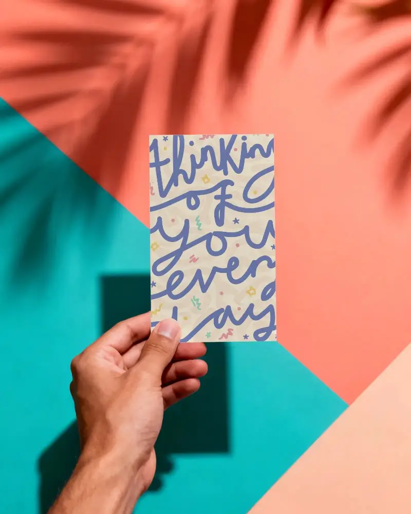 Isolated Vertical Greeting Card Mockup Held In Hand With Sharp Shadow On Color Block Surface