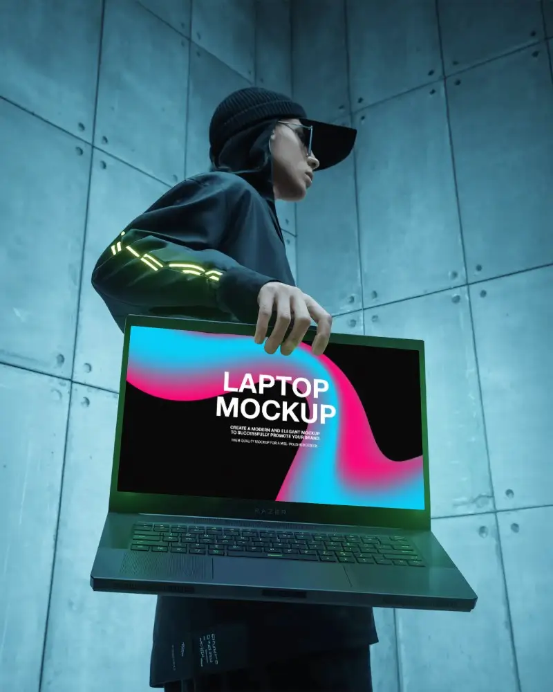 Razer Gaming Laptop Mockup Held By Person In Cyberpunk Outfit Against Industrial Grey Wall Backdrop