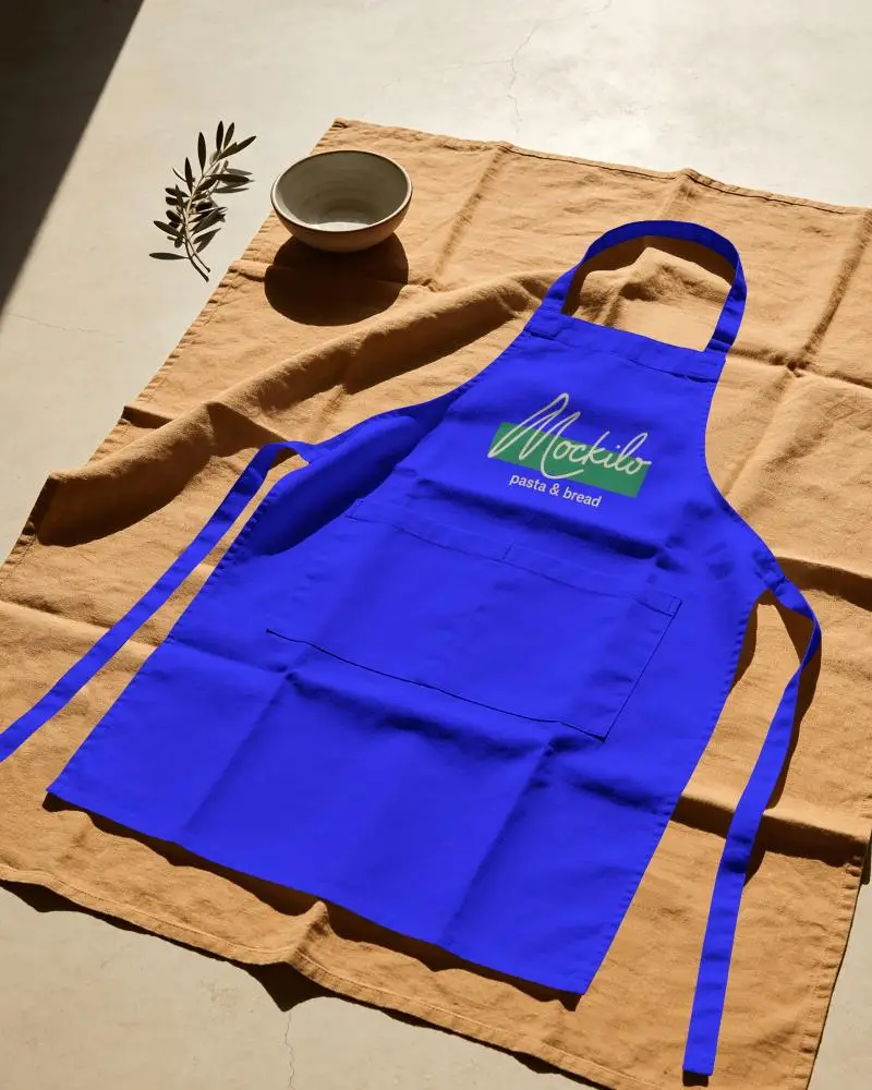 Sunlit Flat Lay Chef Apron Mockup On Rustic Cloth With Ceramic Bowl And Olive Sprig
