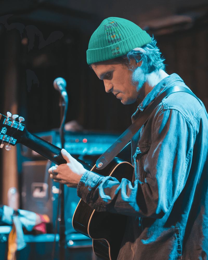 Moody Live Music Beanie Mockup Male Guitarist In Denim Jacket Under Blue Stage Lighting Intimate Concert Vibe