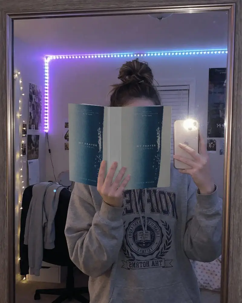 Person Holding Blank Book Mockup In Bedroom Mirror Taking Selfie For Promo Post