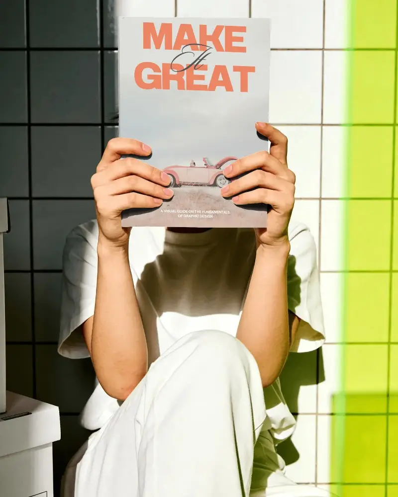 Person Holding Blank Book Cover Mockup Against Tiled Wall Background In Light