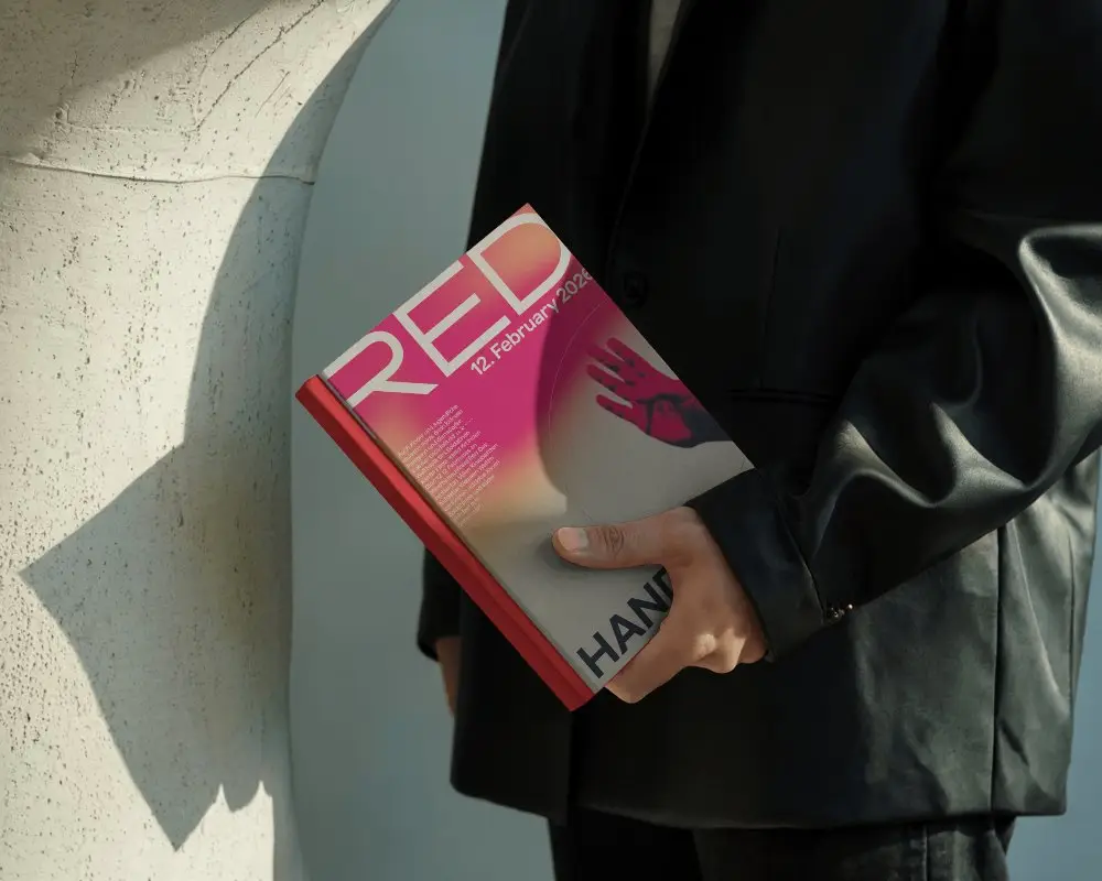 Person Holding Hardcover Book Mockup With Creased Pages Wearing Dark Coat Outdoor Shadows On Cover