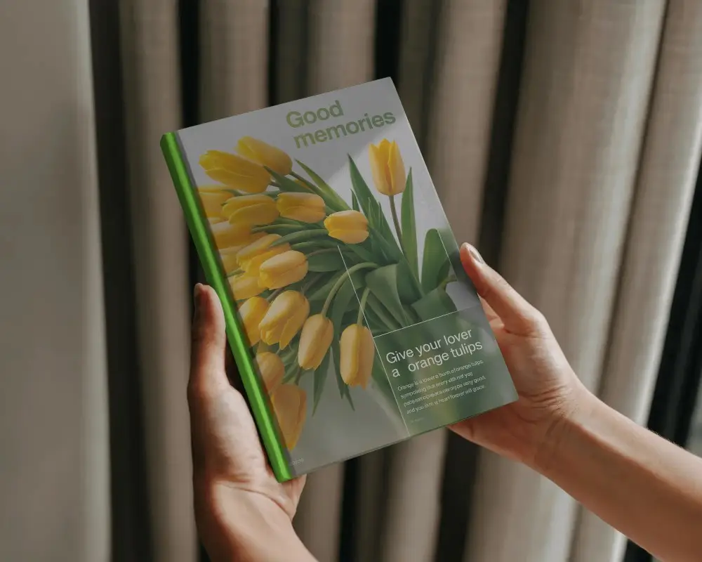 Hardcover Book Mockup Hands Lifting Book In Cozy Indoor Lighting With Curtain Backdrop