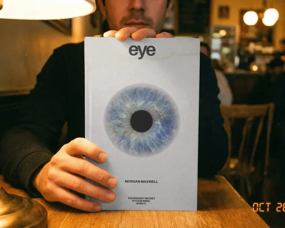 Man Holding Hardcover Book Mockup On Wooden Table In Cozy Ambient Cafe Setting