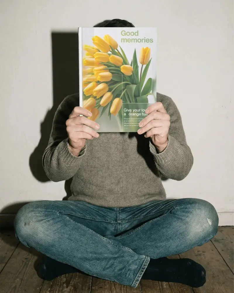 Seated Person Holding Blank Book Cover Mockup In Front Of Face Isolated Minimalist Background