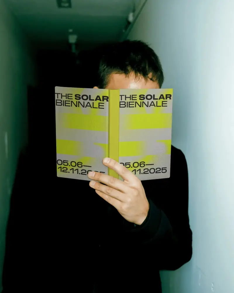 Person Standing In Narrow Hallway Holding Open Book Cover Front Facing Camera