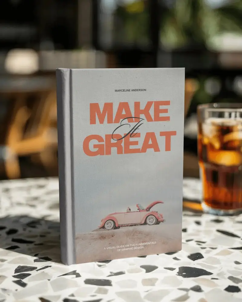 Hardcover Book Mockup On Terrazzo Cafe Table With Iced Drink In Bright Daylight