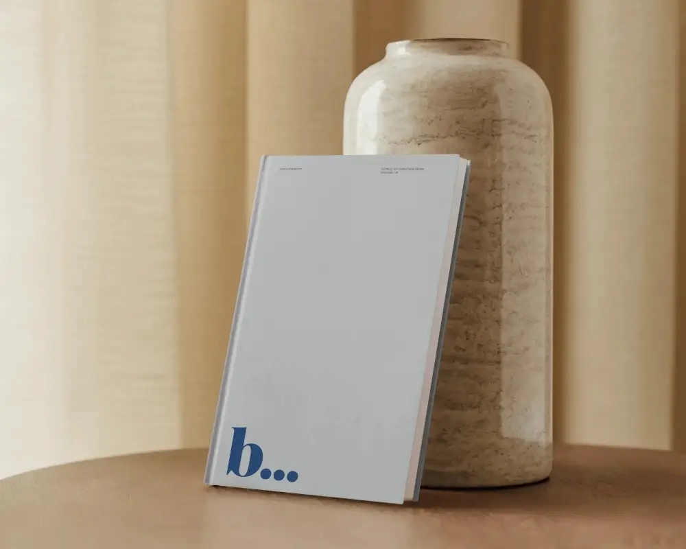 book-mockup-against-ceramic-vase-and-curtains-on-wooden-surface-soft-earthy-lighting