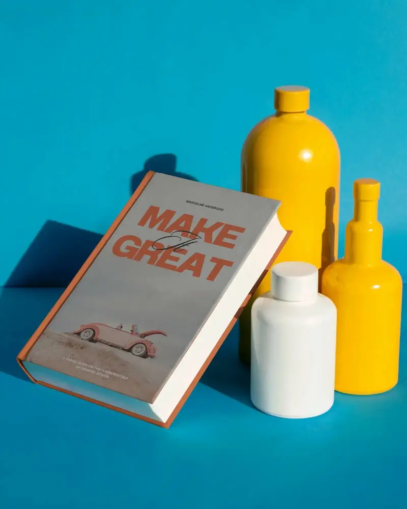 Hardcover Book Mockup Floating Among Cylindrical Bottles On Bright Surface Background