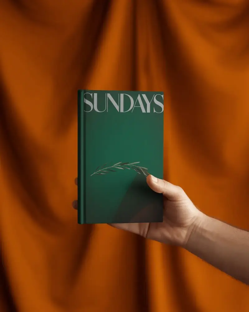 Hand Holding Hardcover Book Mockup Against Draped Orange Fabric Studio Background