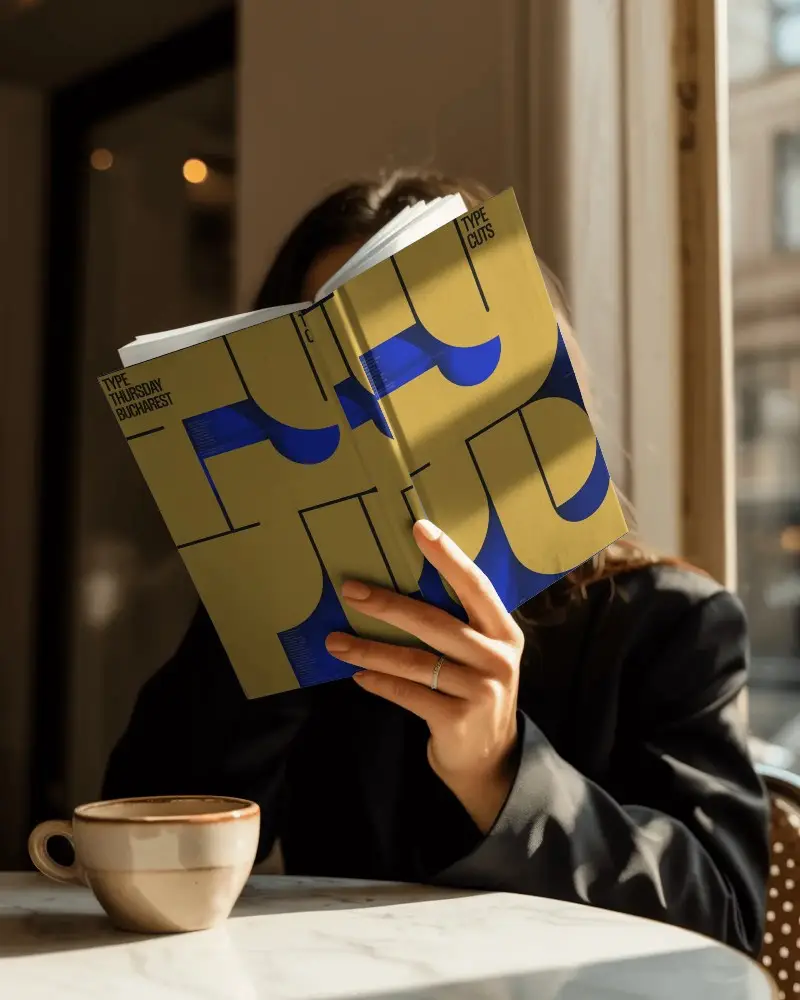 Woman Reading Hardcover Book Mockup At Cozy Cafe Table With Coffee Cup And Sunlight Window
