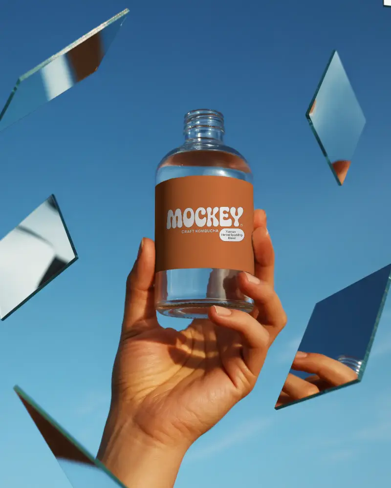 Hand Holding Clear Empty Glass Bottle With Black Label Against Blue Sky Background