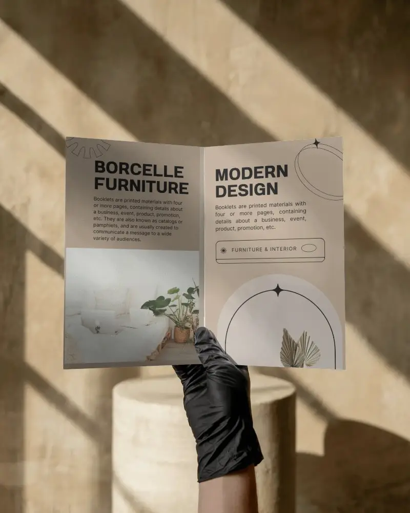 Hand Holding Open Bi Fold Brochure Mockup In Sunlit Minimal Interior With Soft Shadows And Earthy Background For Modern Presentation