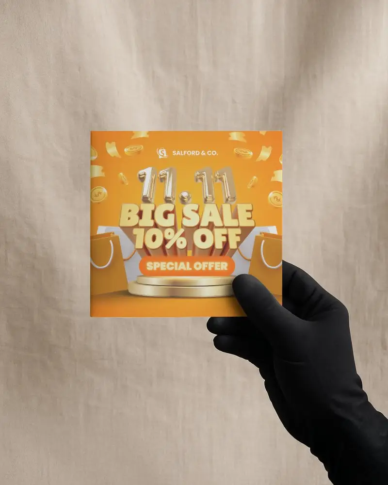 Hand Holding Square Brochure Mockup In Front Of Plain Fabric Backdrop Promotional Scene For Retail Discount Campaign Presentation