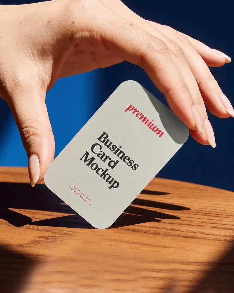 Minimalist Vertical Rounded Corners Business Card Mockup Held By Hand Above Wooden Surface