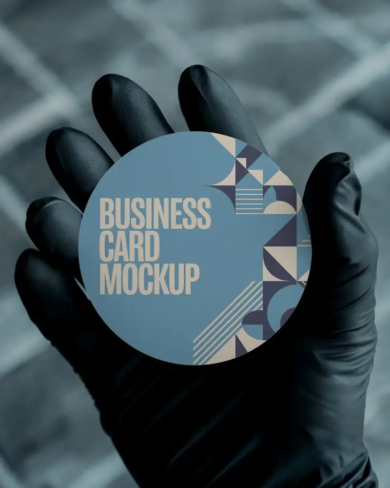 Hand Holding Round Business Card Mockup In Black Glove With Paved Stone Background And Focus Depth