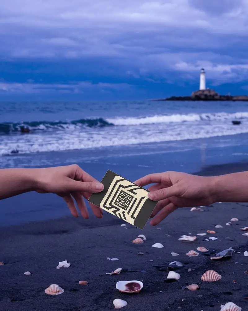 Twilight Beach Business Card Mockup Hands Holding Card Over Shell Covered Sand With Lighthouse In Distance Moody Coastal Setting 0164