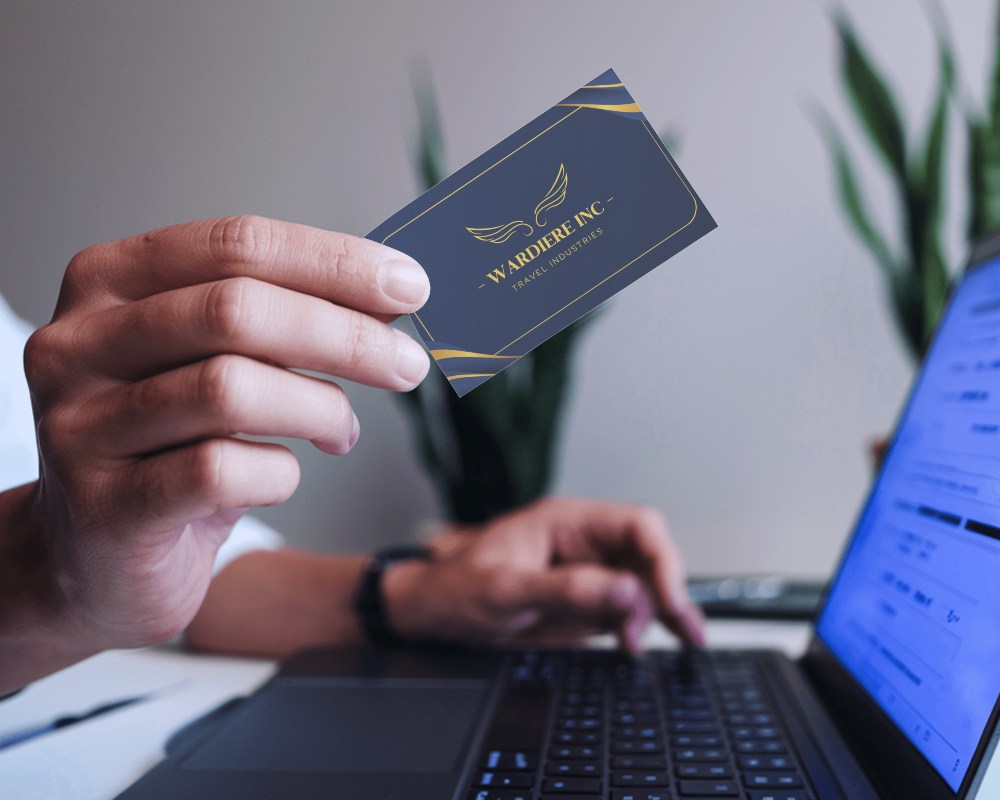 Close Up Hand Holding Business Card In Office Setting Focused On Card Display With Laptop In Background