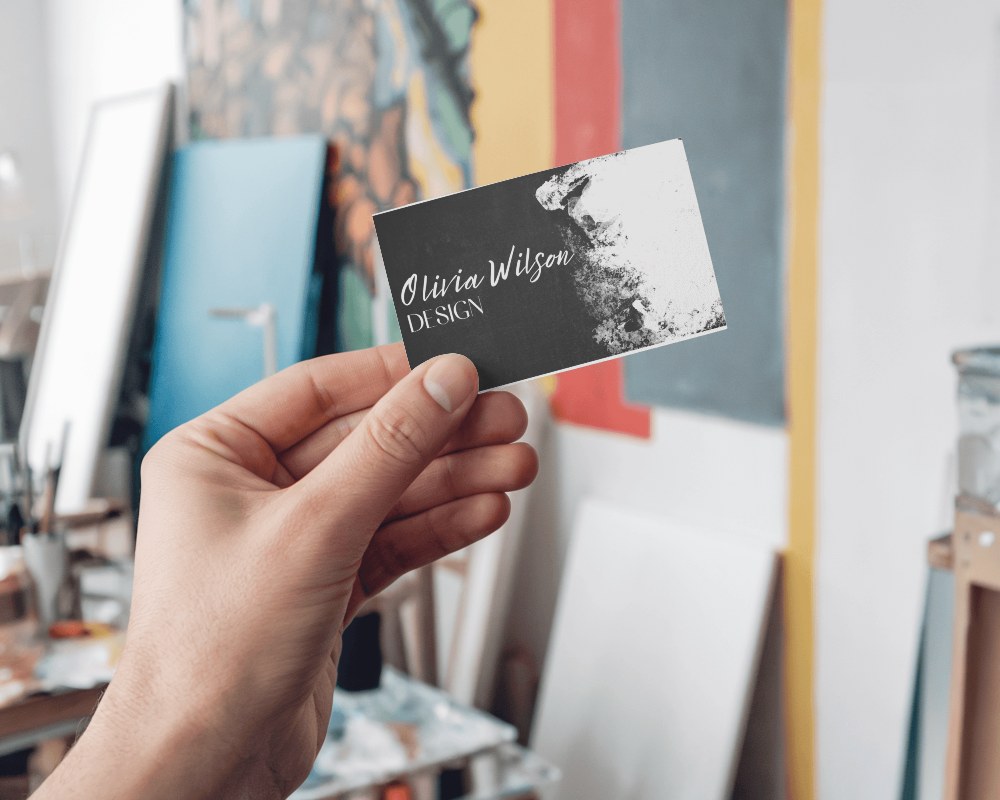 Creative Studio Business Card Mockup Hand Holding Card Against Artistic Backdrop With Soft Light