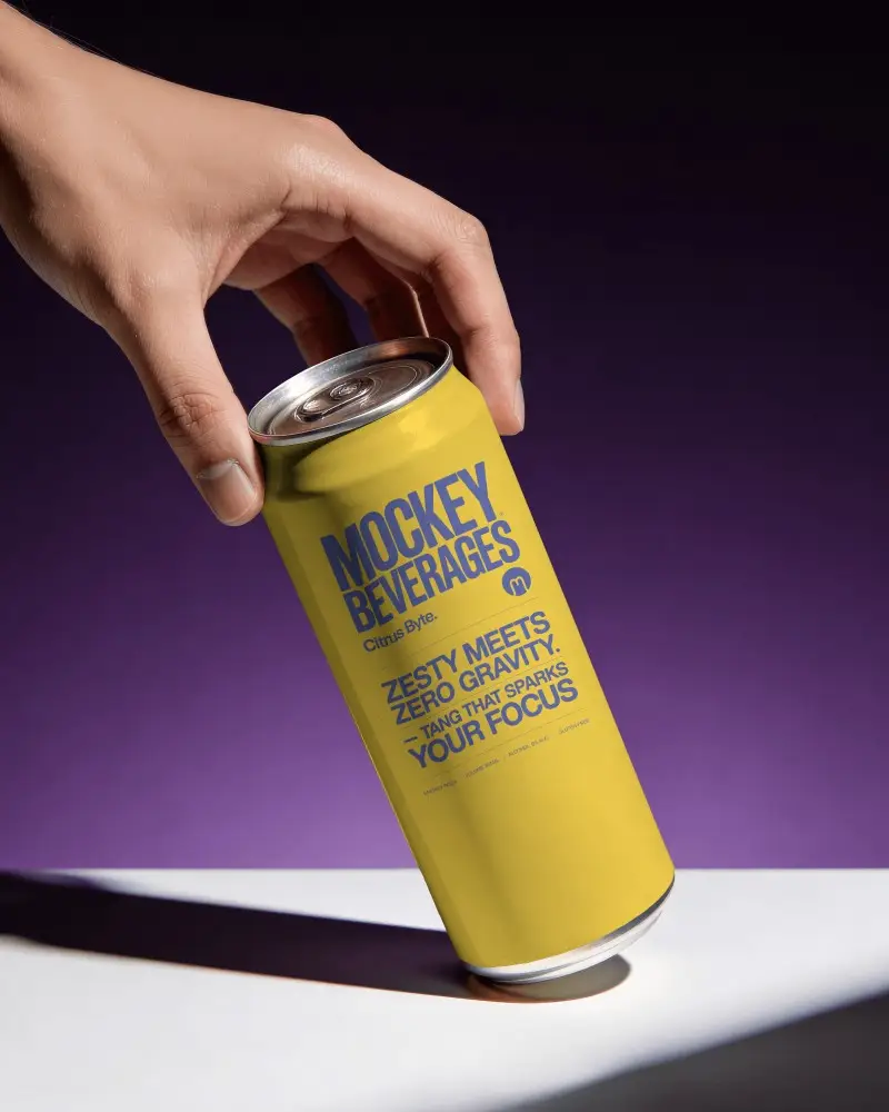 Hand Placing Soda Can Mockup On White Surface With Purple Studio Background And Dramatic Shadow