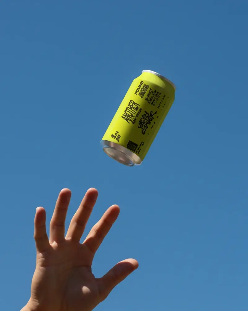 Hand Releasing Empty Can Mockup Against Clear Blue Sky Background For Branding