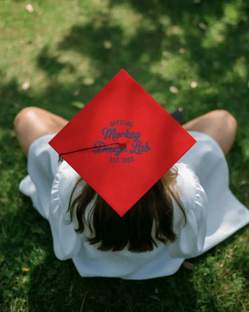 Graduation Cap Mockup On Student Sitting In Sunlit Grass From Top View