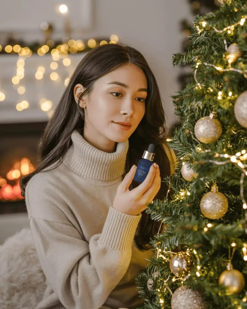 Holiday Dropper Bottle Mockup Female Model By Christmas Tree With Golden Lights