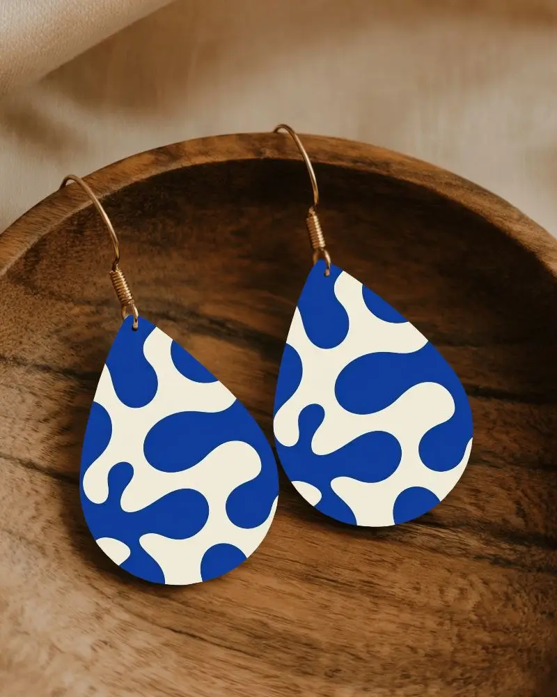 Elegant Black Teardrop Earrings Hanging On Golden Hooks Sitting On Wooden Bowl With Soft Lighting