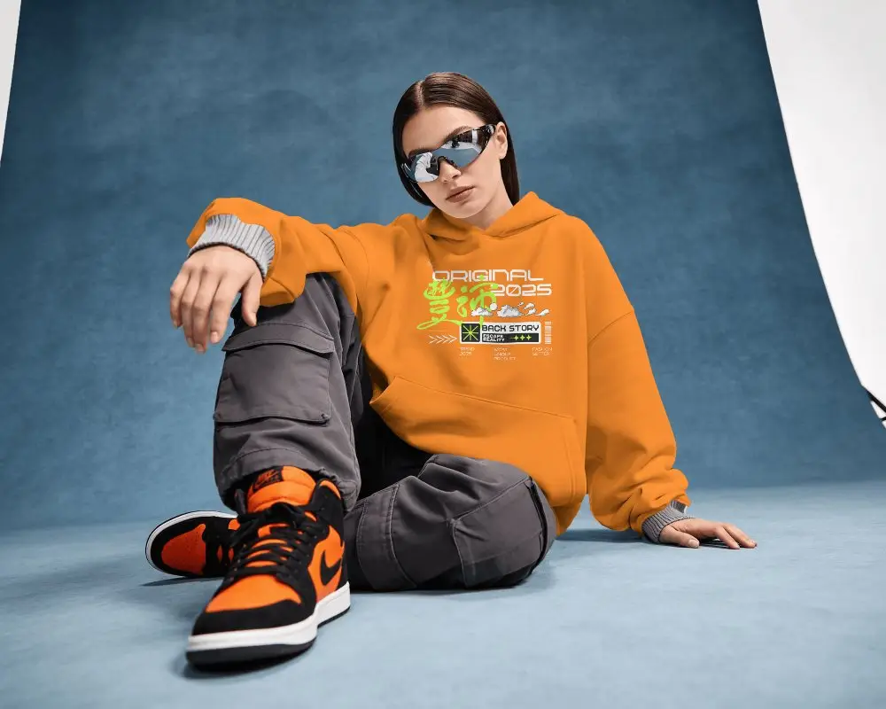 Seated Hoodie Mockup Female Model Posing On Studio Floor With Sunglasses And Bold Attitude