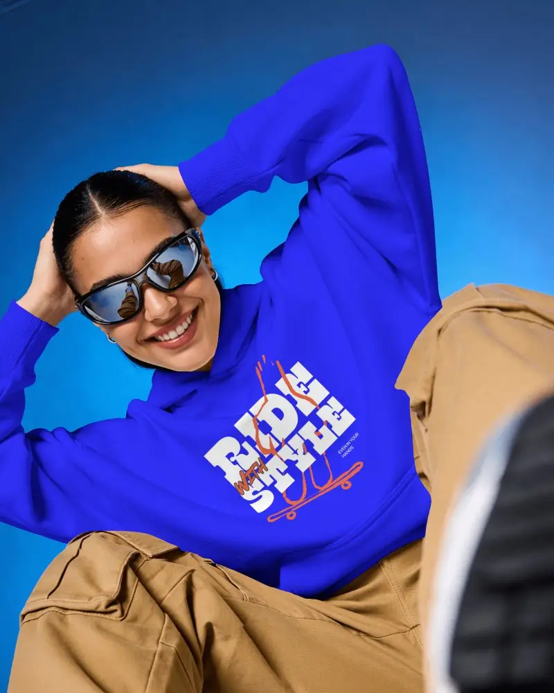 Low Angle Hoodie Mockup Female Model Smiling With Sunglasses In Bold Blue Studio Playful Energy