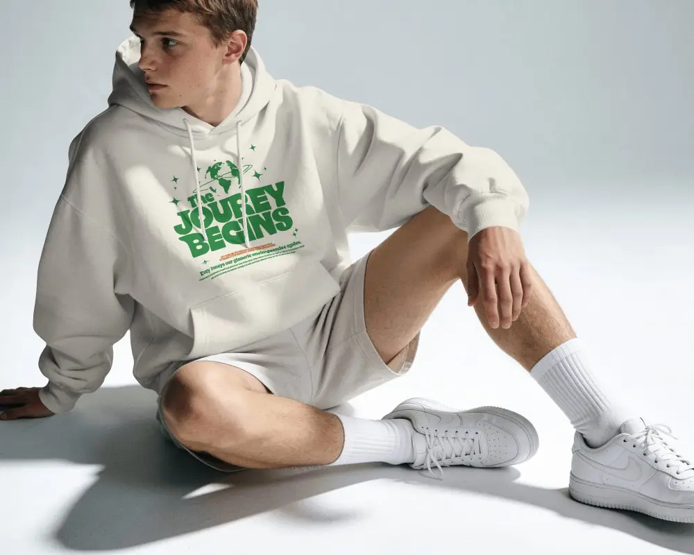 Seated Male Model Hoodie Mockup With One Knee Raised And Sideward Gaze In Hard Studio Light