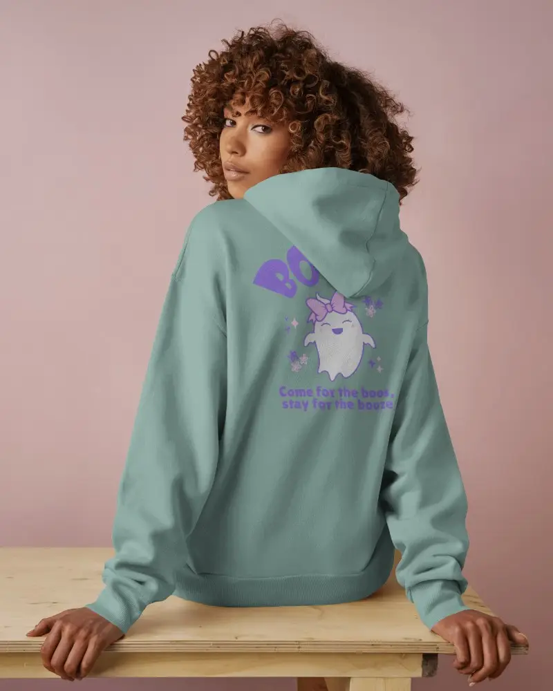Back View Hoodie Mockup With Female Model Sitting On Wooden Table Against Soft Pink Background