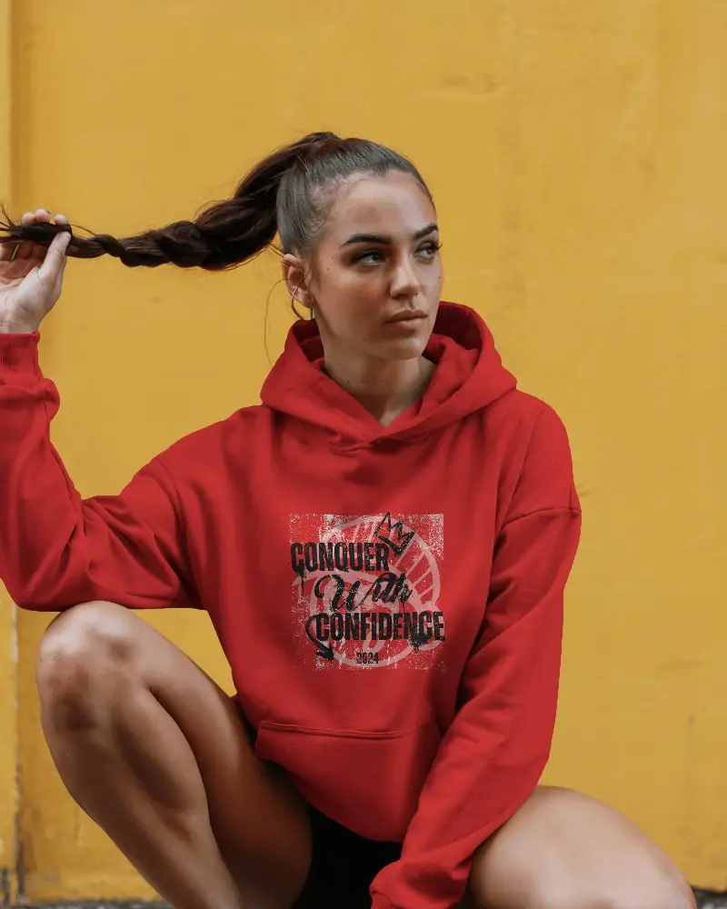 Sporty Feminine Hoodie Mockup In Natural Light Featuring Model Sitting On Ground In Modern Urban Environment
