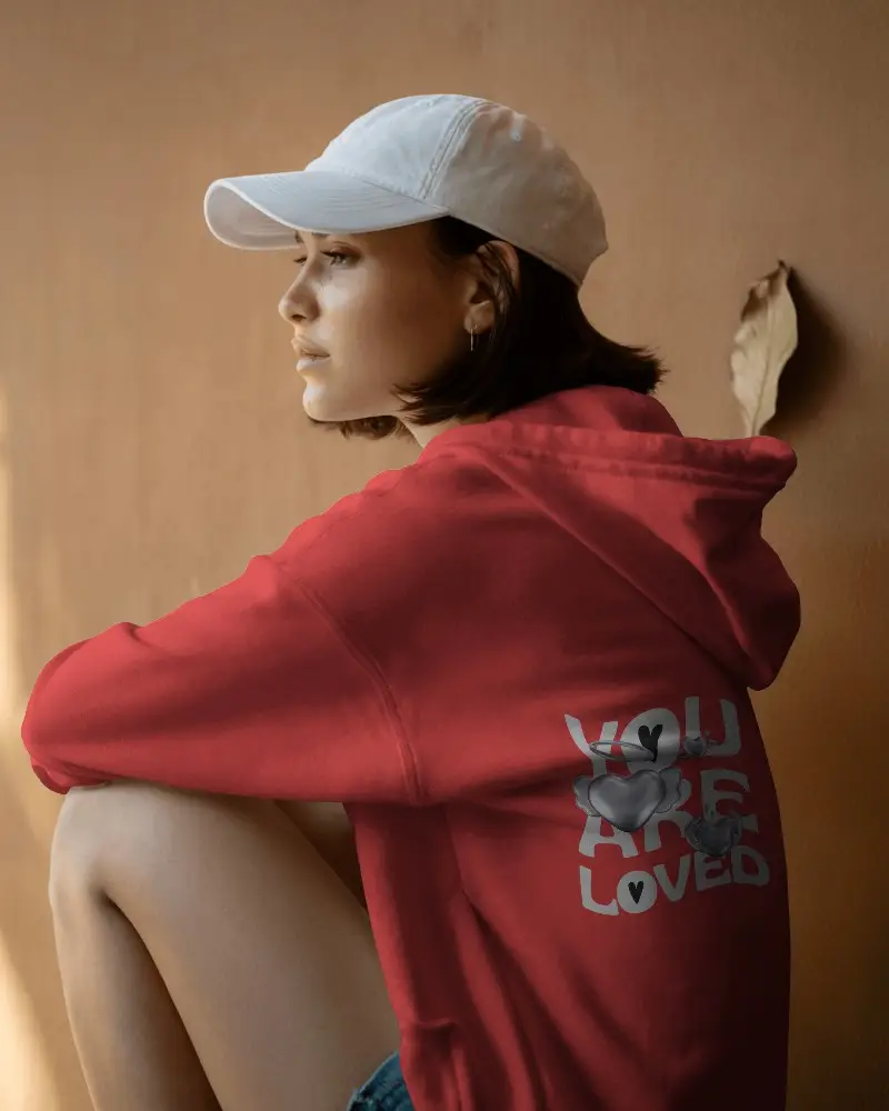 Moody Outdoor Hoodie Mockup Female Model Wearing Cap Sitting Against Earth Toned Wall In Natural Light 0530