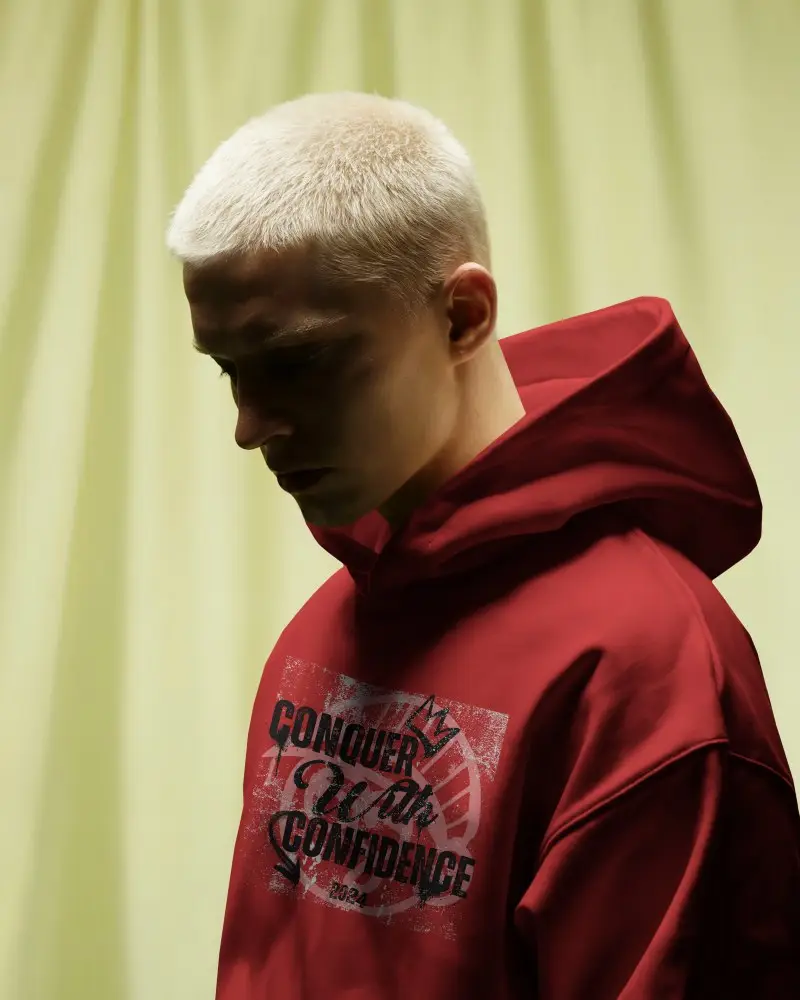 Moody Studio Hoodie Mockup Blonde Male Model Looking Down Against Soft Yellow Curtain Backdrop