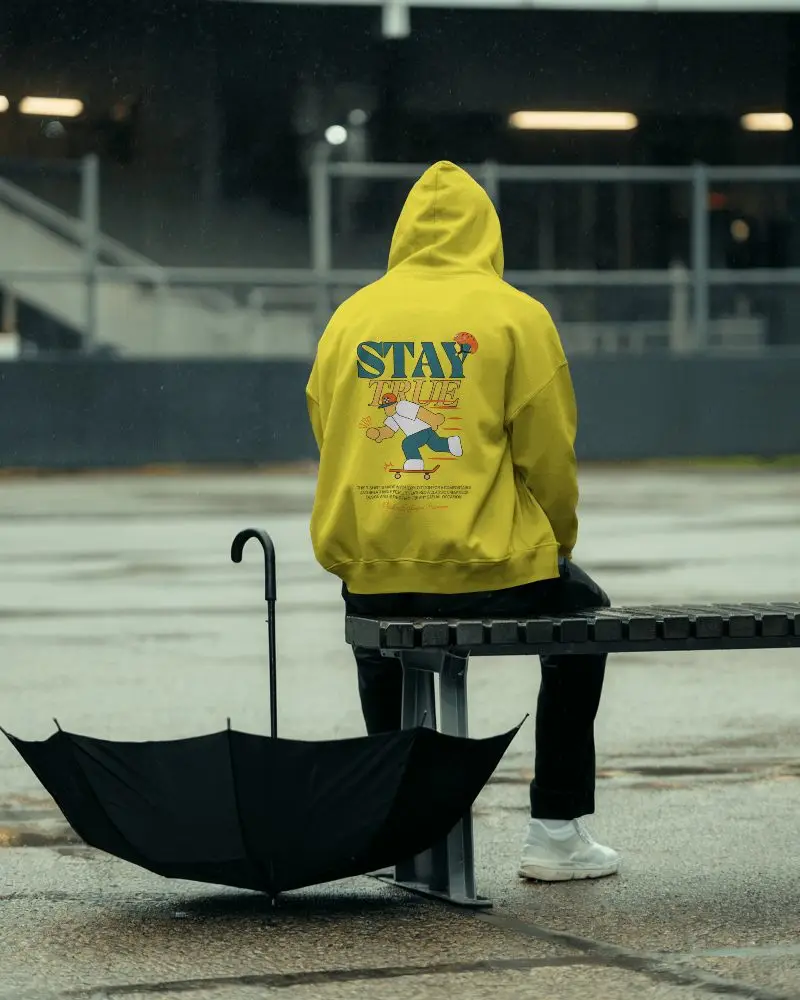 Rainy Day Hoodie Mockup Person Sitting On Metal Bench With Open Umbrella Moody Outdoor Setting 0789