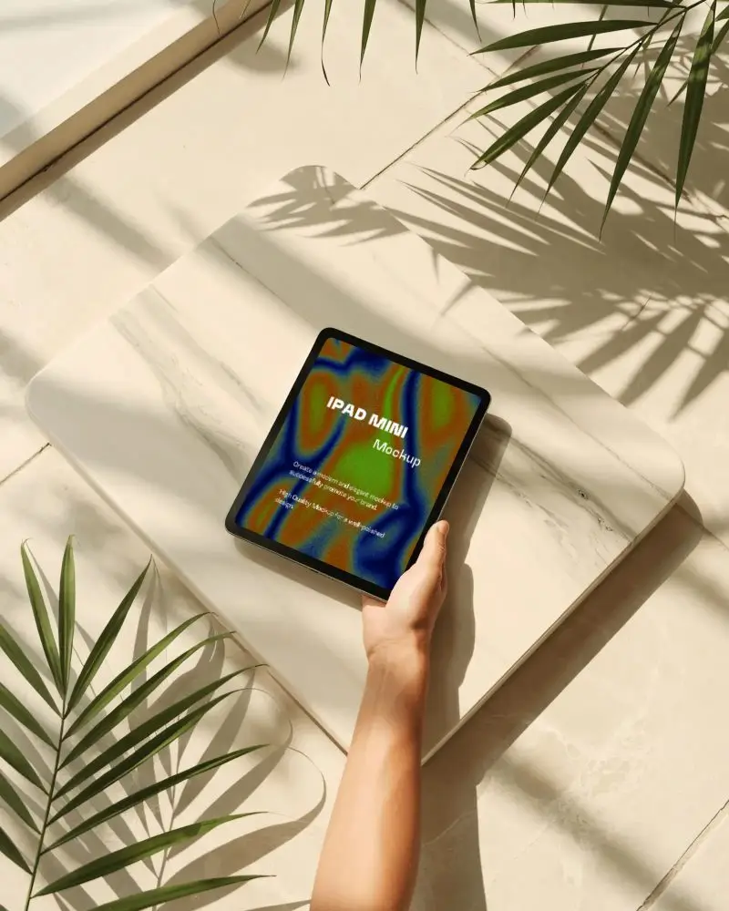 ipad-mini-mockup-on-marble-platform-with-hand-holding-and-sunlit-tropical-leaf-shadows