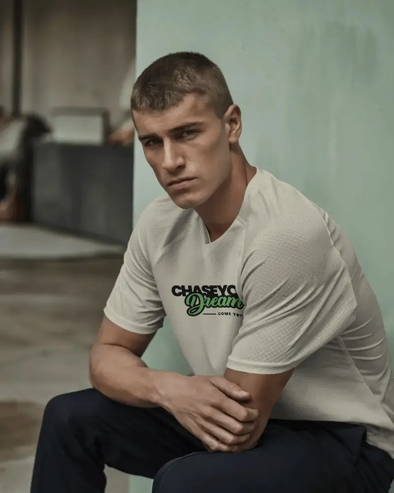 Urban Sportswear Jersey Mockup With Male Model Sitting Against Concrete Wall In Relaxed Pose Showcasing Front Chest Design For Custom Branding