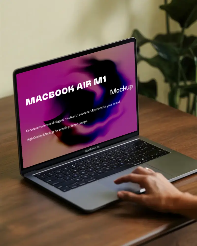 Macbook Air M1 Mockup Hand On Trackpad Wooden Desk Indoor Natural Light Soft Focus Background Green Houseplant Modern Creative Setup