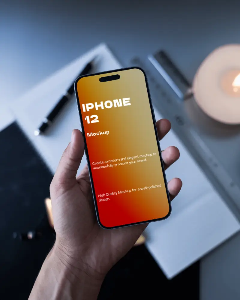 Hand Holding Iphone 12 Mockup Above Desk With Office Supplies