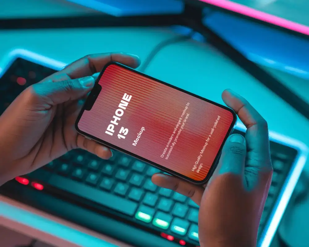 Iphone 13 Mockup In Hands Horizontal View Over Rgb Gaming Keyboard With Neon Lighting