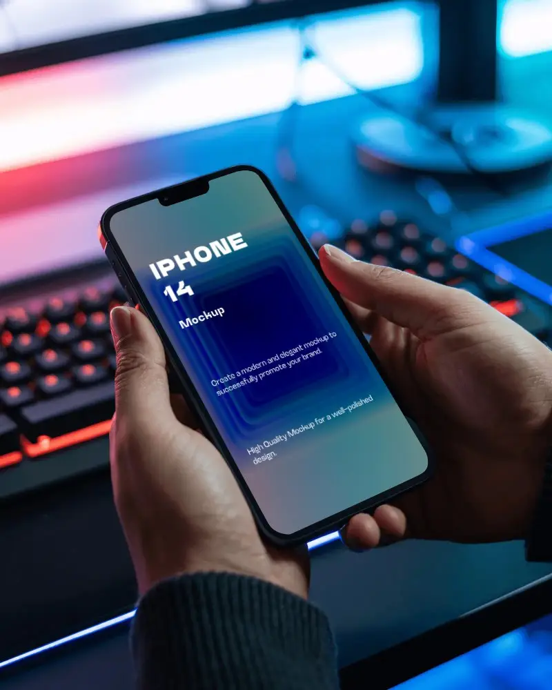 Person Holding Modern Iphone 14 Mockup With Blurred Gaming Keyboard Background For App Preview