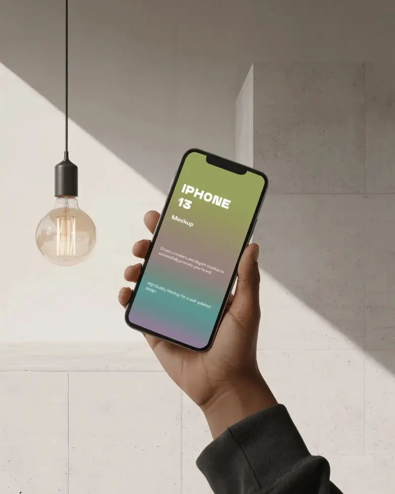 Hand Holding Iphone 13 Mockup Under Warm Lightbulb With Minimal Stone Wall Background