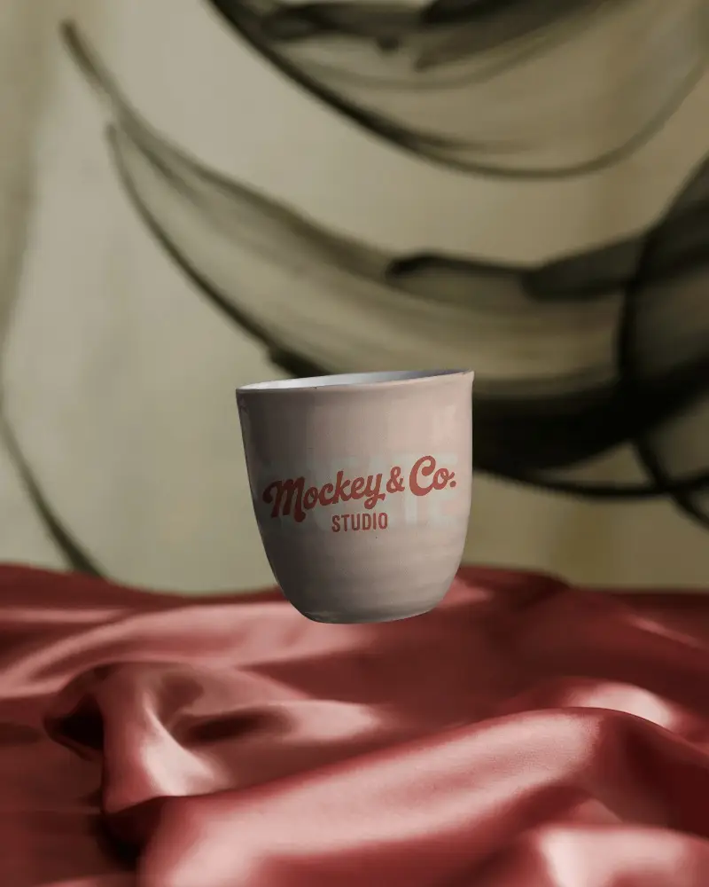 Minimalistic Ceramic Mug Floating Above Satin Fabric With Modern Abstract Art Backdrop