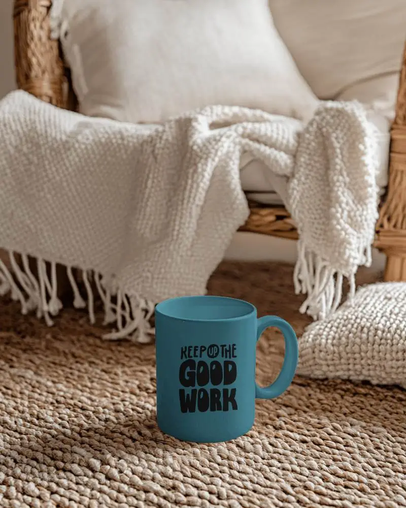 Cozy Living Room Mug Mockup White Ceramic Mug On Textured Rug Next To Wicker Chair With Comfy Blanket And Pillows In A Relaxed Home Setting