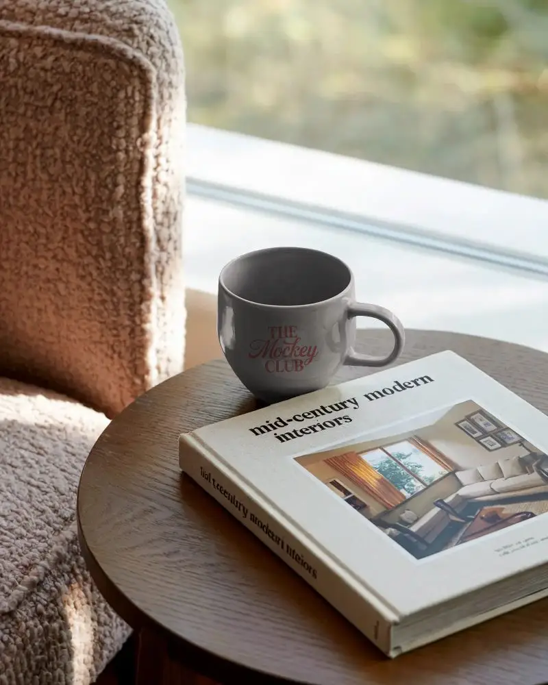Elegant Ceramic Coffee Mug Mockup Next To Mid Century Interior Book On Table
