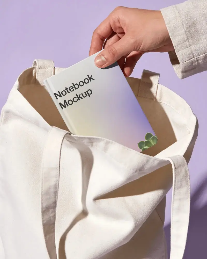 Portable Hardcover Notebook Being Put Into Large Canvas Tote Bag For Easy Carry