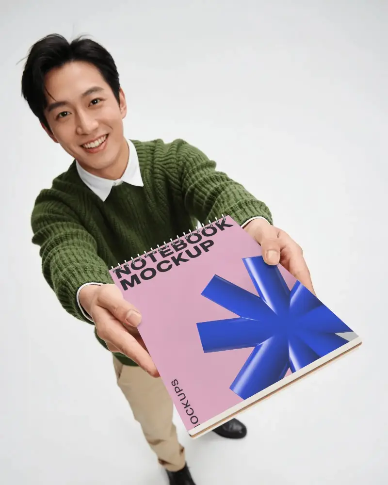 Foreshortened Handheld Notebook Mockup With Young Man Extending Sketchbook In Clean Studio