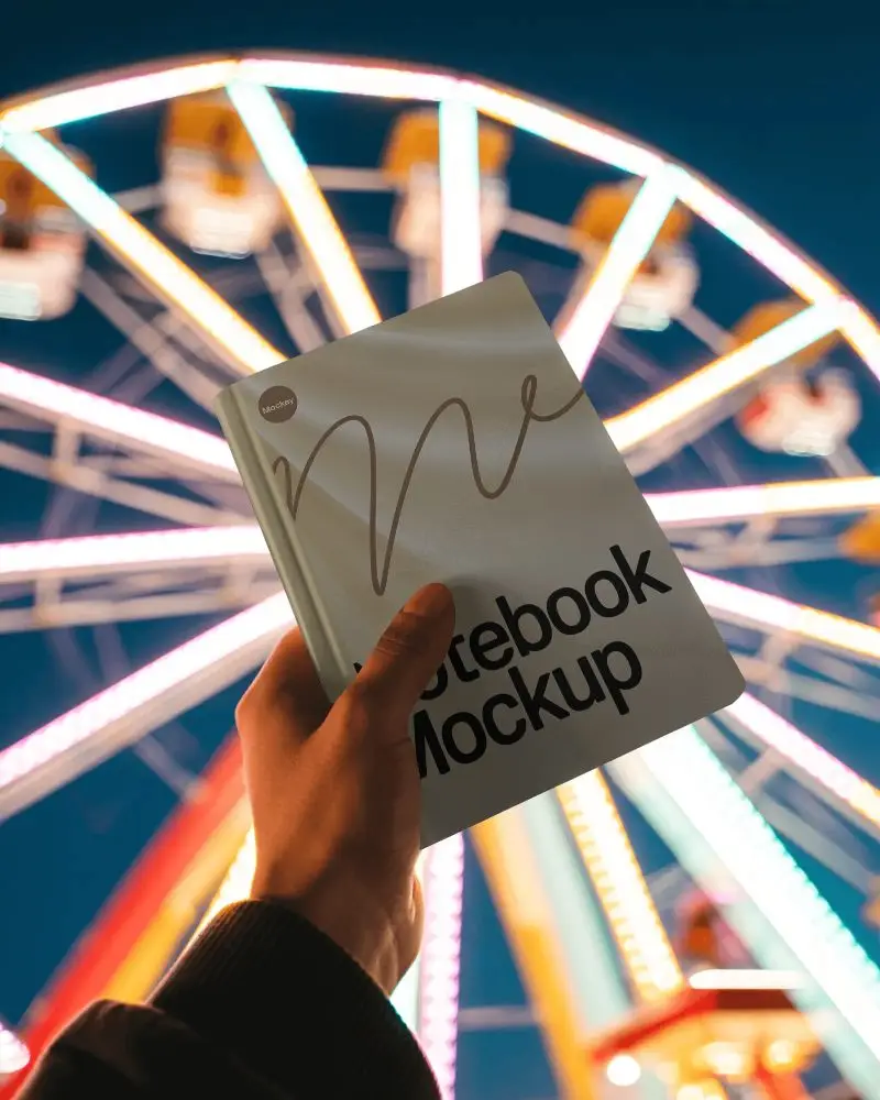Night Fair Notebook Mockup Held Up With Bright Ferris Wheel Lights In Background